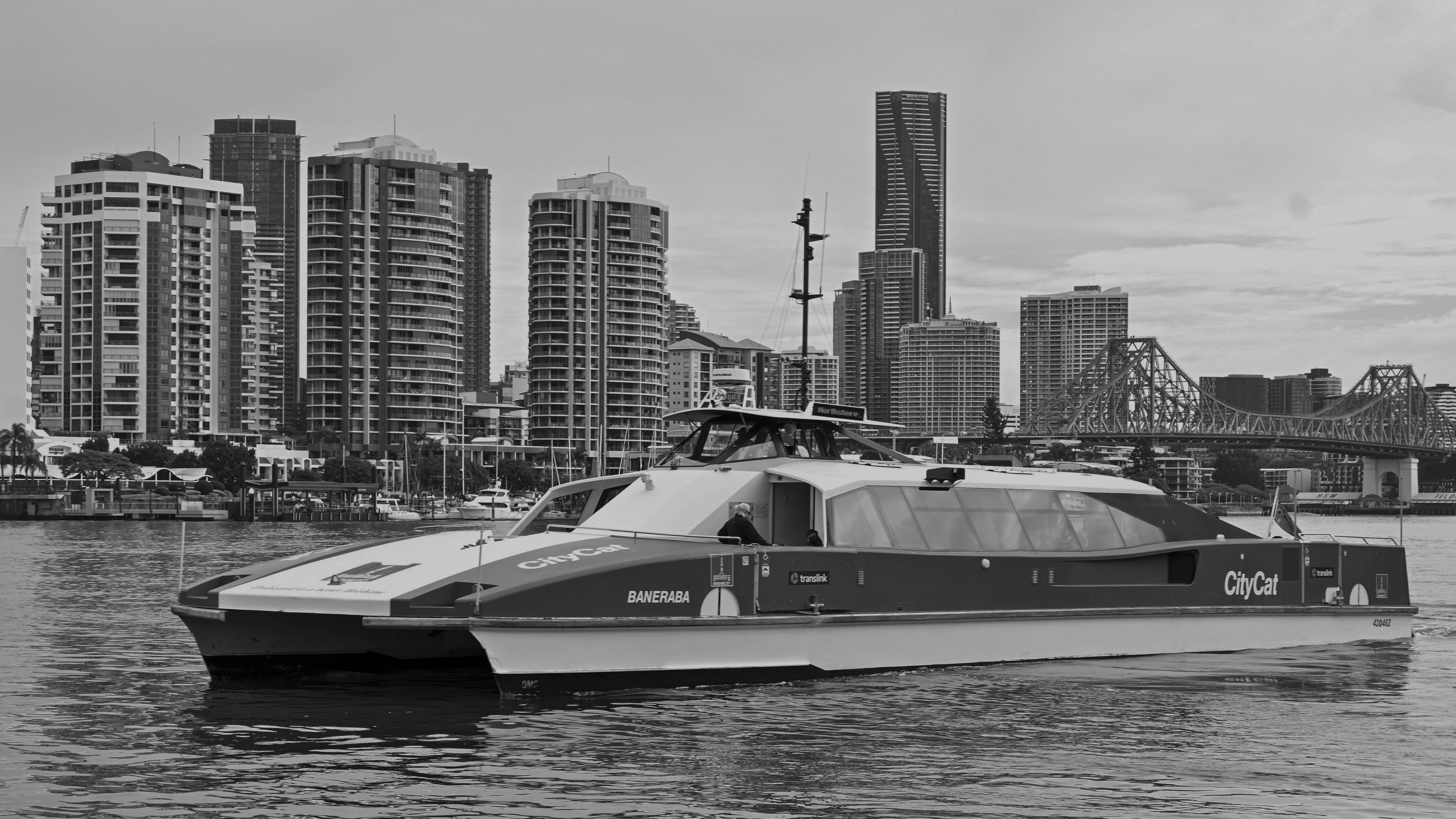 Black and white image of Brisbane's CityCat ferry with the urban skyline in the background.