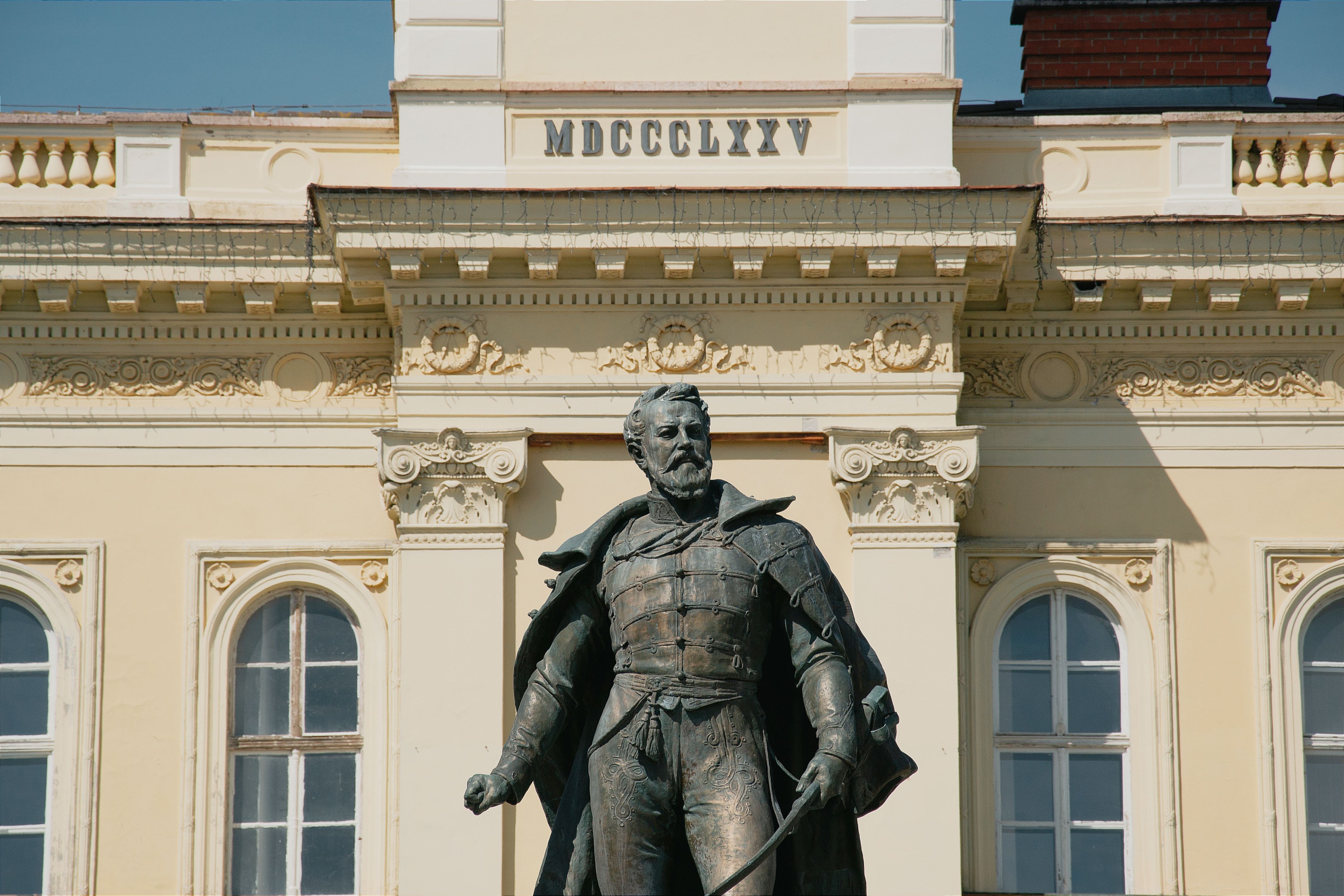 A detailed view of a historic statue against a classical facade in Komárno, Slovakia.