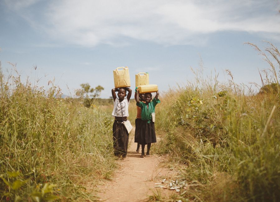 Two children walking through a rural pathway carrying water containers on their heads in Kitgum, Uganda.