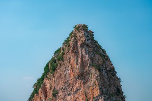 A majestic rocky cliff rises against a clear blue sky, creating a stunning outdoor landscape.