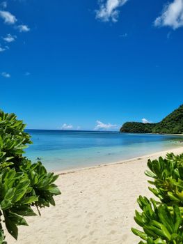 Pristine tropical beach with turquoise waters and lush greenery under a bright blue sky.