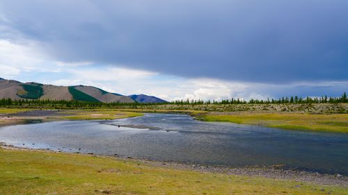 Free A tranquil river flows through a scenic landscape with green hills and a clear blue sky. Stock Photo