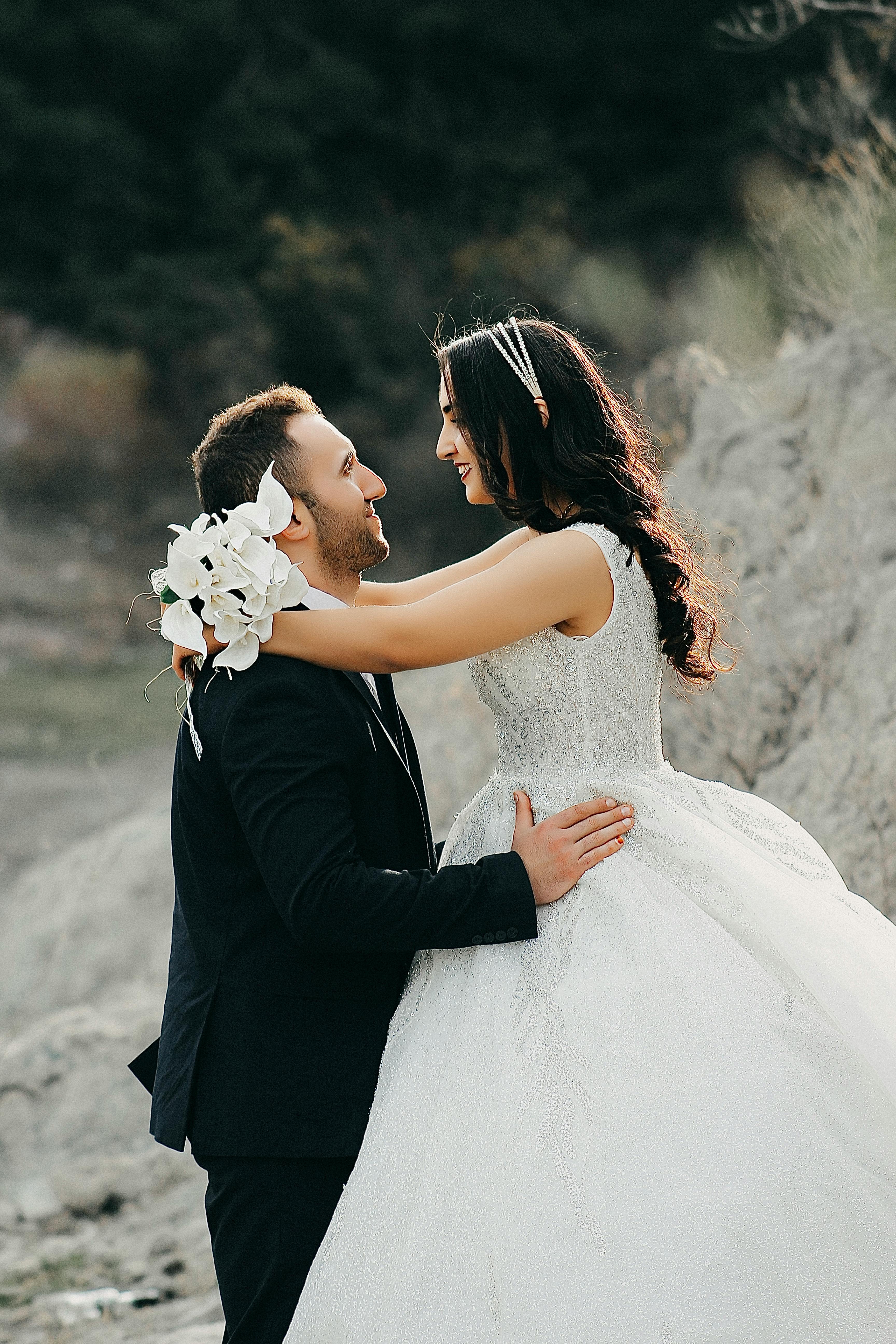 a bride and groom embrace in front of a rocky shore