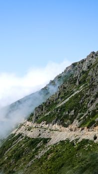 Breathtaking view of a mountainside pathway enveloped by mist and clouds under a clear sky.