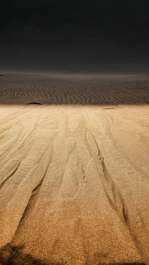 Free A mesmerizing view of rippling sand dunes under dramatic lighting in a vast desert setting. Stock Photo