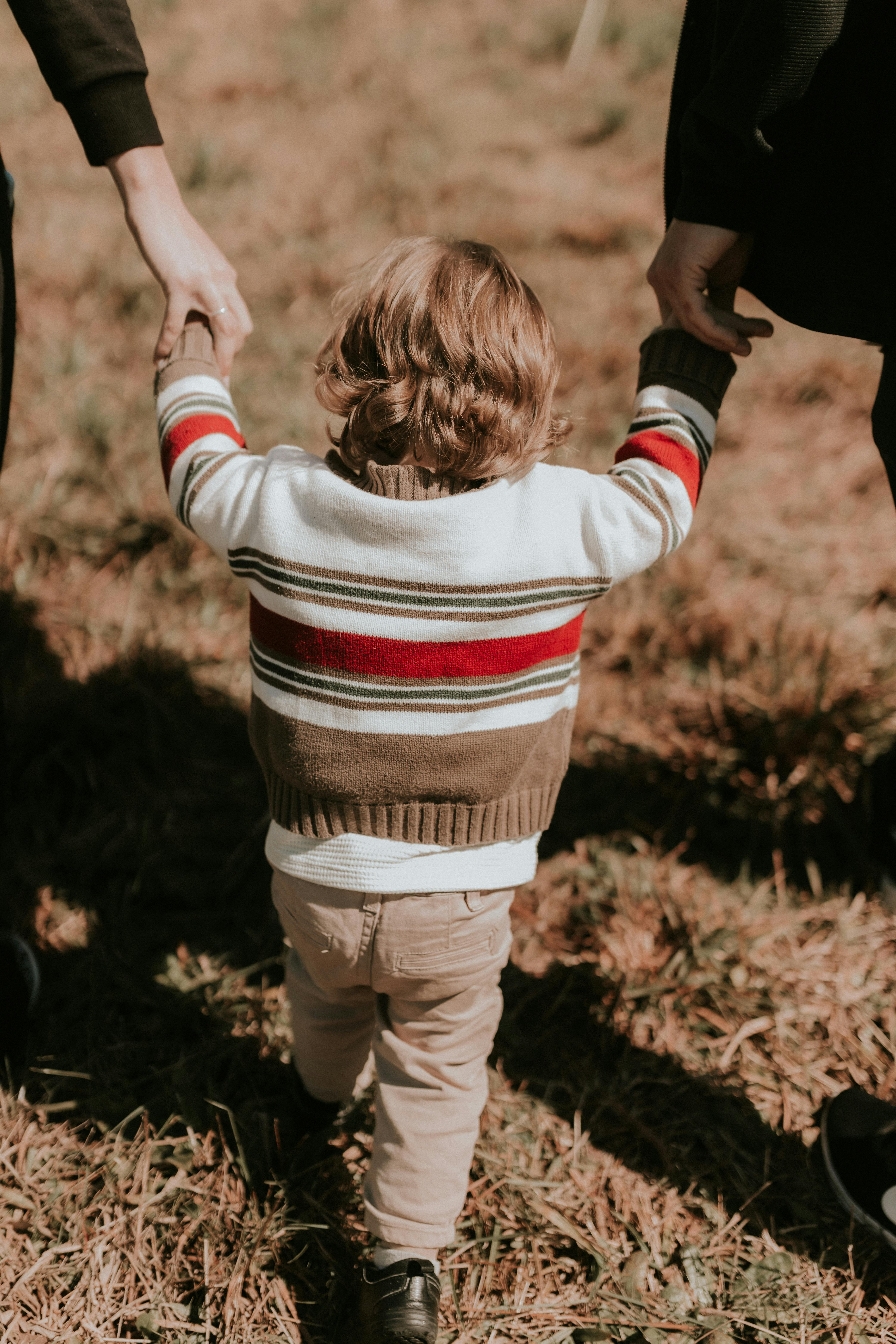 A young child walking hand in hand with adults in a park, conveying family bonding.