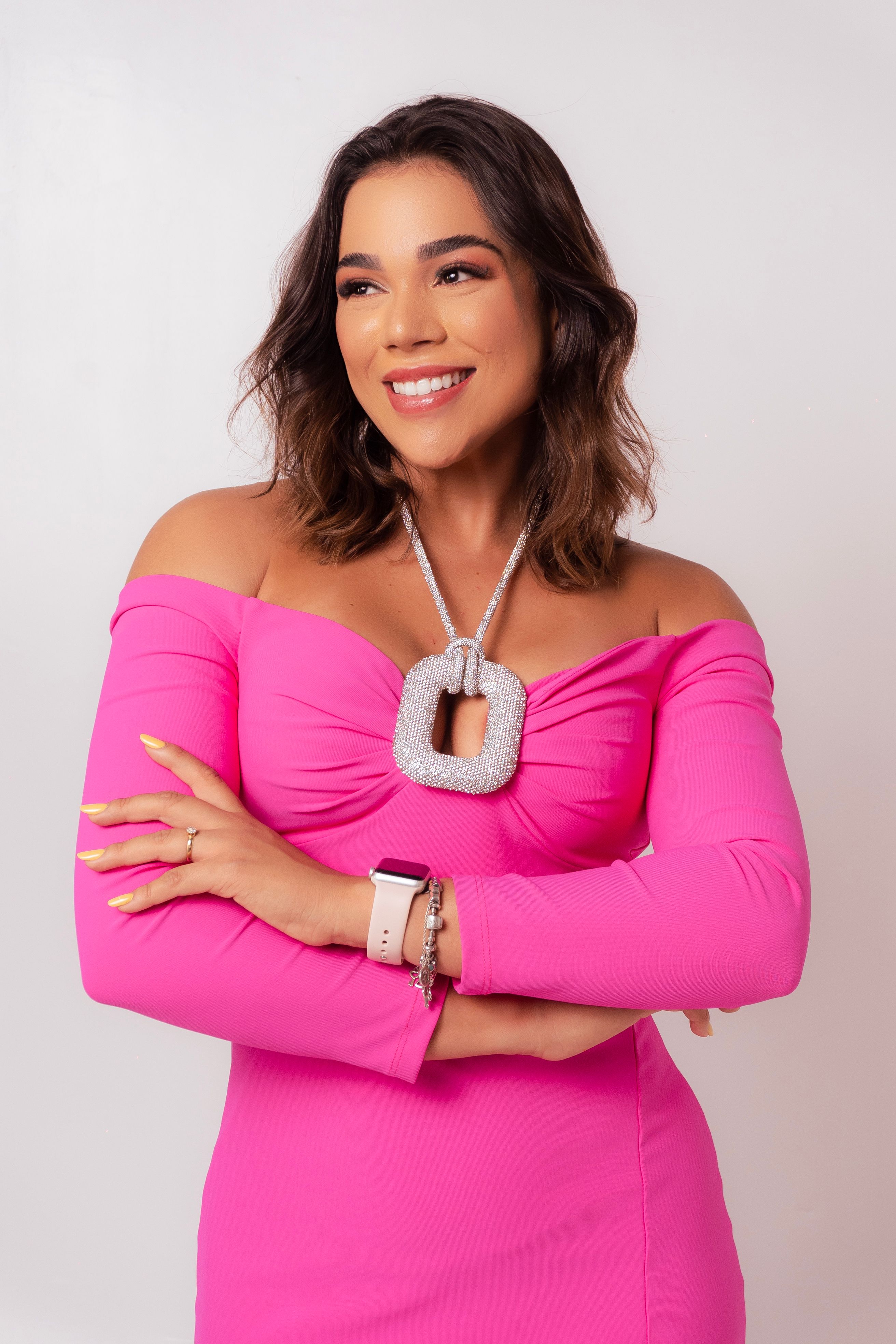 A confident woman poses in a vibrant pink dress, smiling warmly indoors.