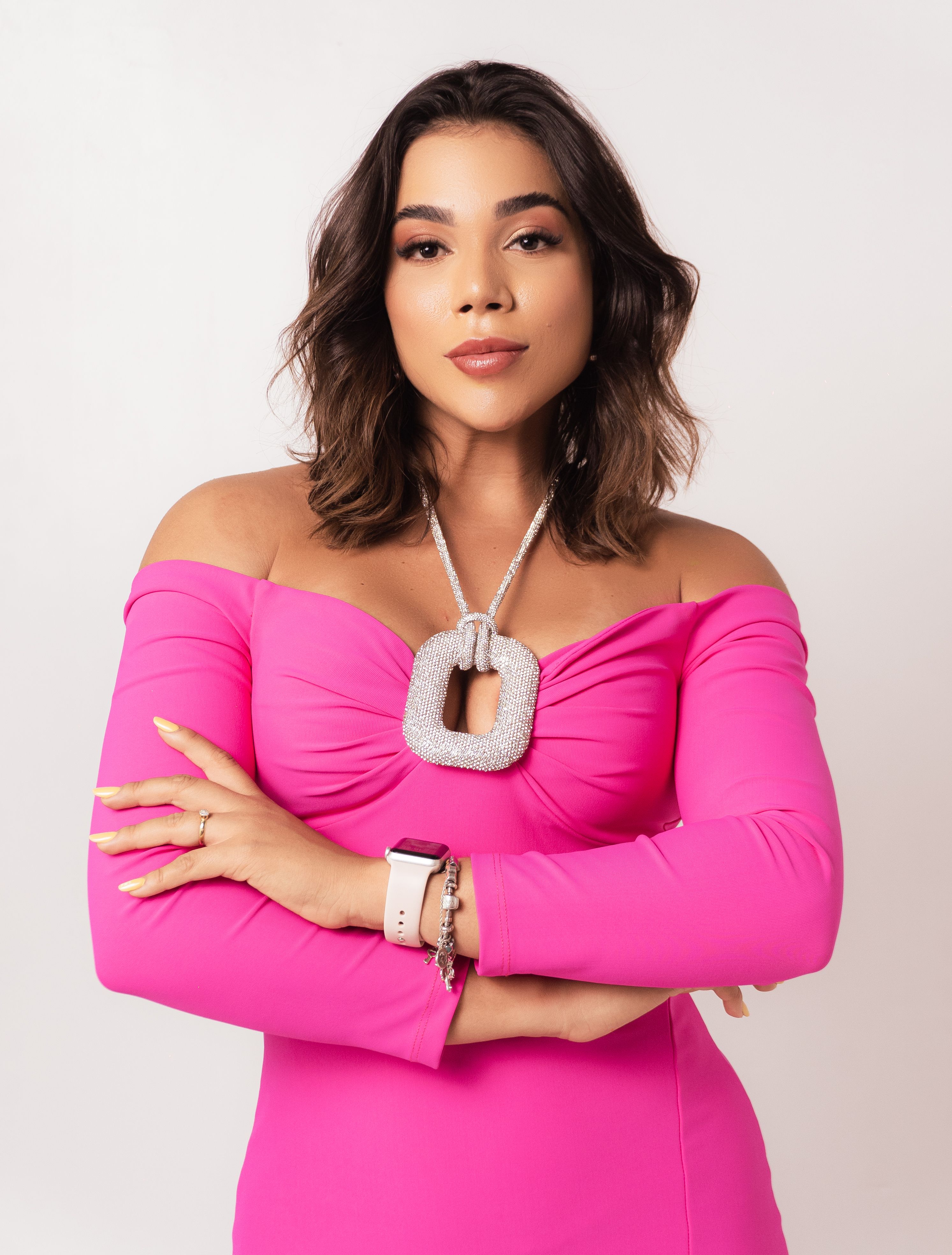 A young woman exuding confidence in a stylish pink off-shoulder dress against a plain background.