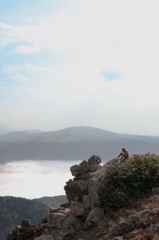 一名孤独的徒步旅行者坐在悬崖边，眺望着壮丽的山景