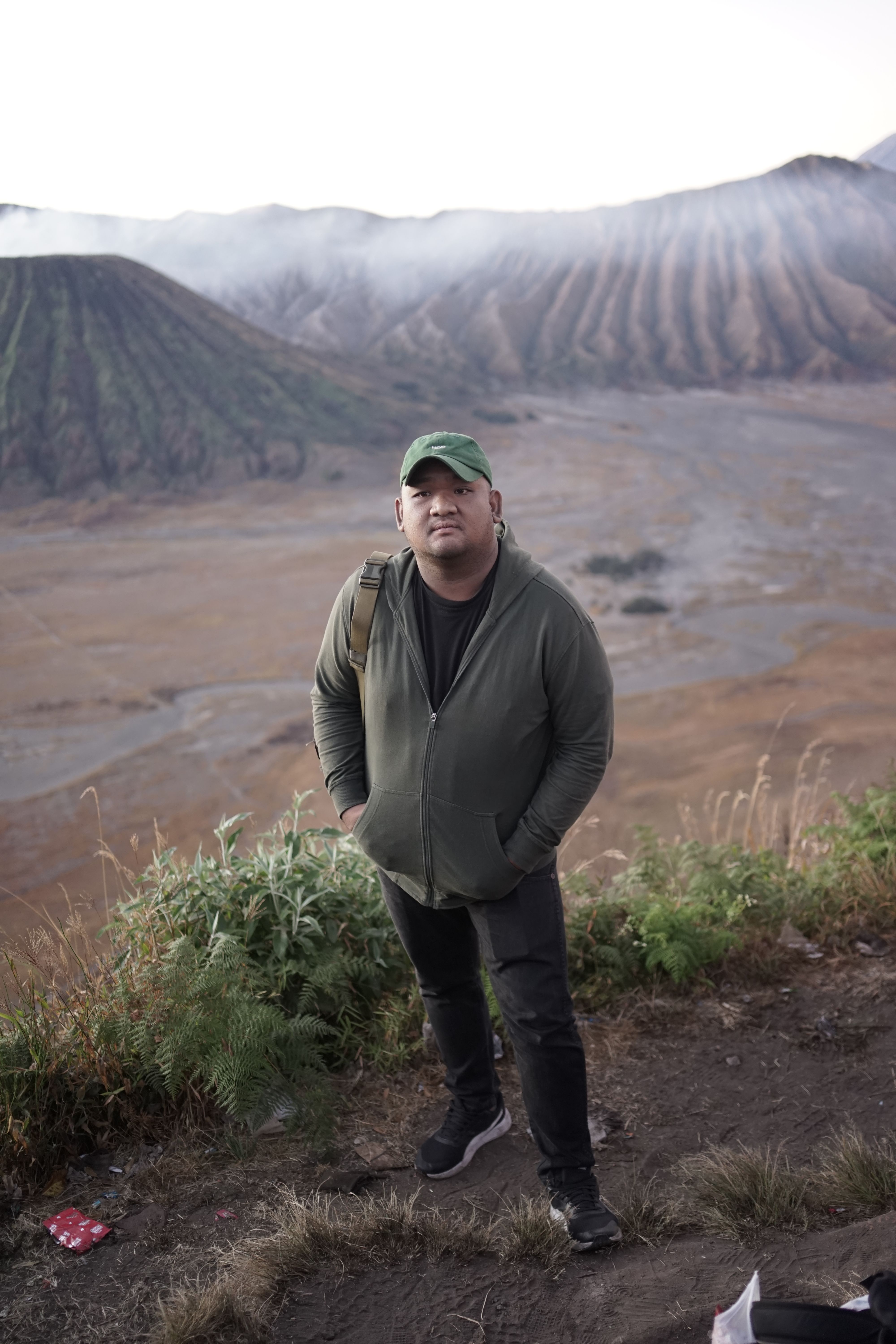 A man stands on a mountain trail with breathtaking scenery in the background.
