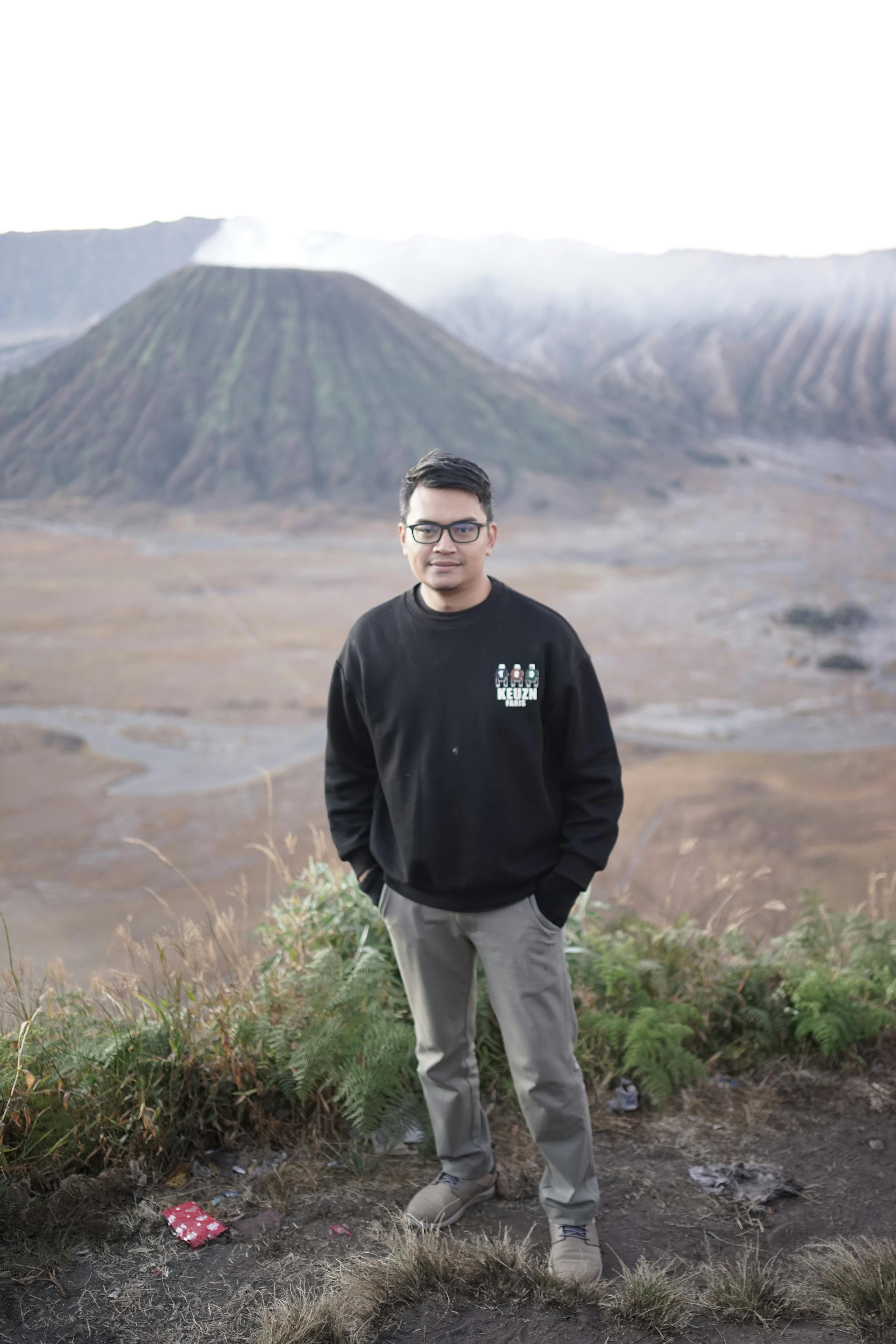 A young man stands in front of Mount Bromo, showcasing adventure and exploration in a volcanic landscape.