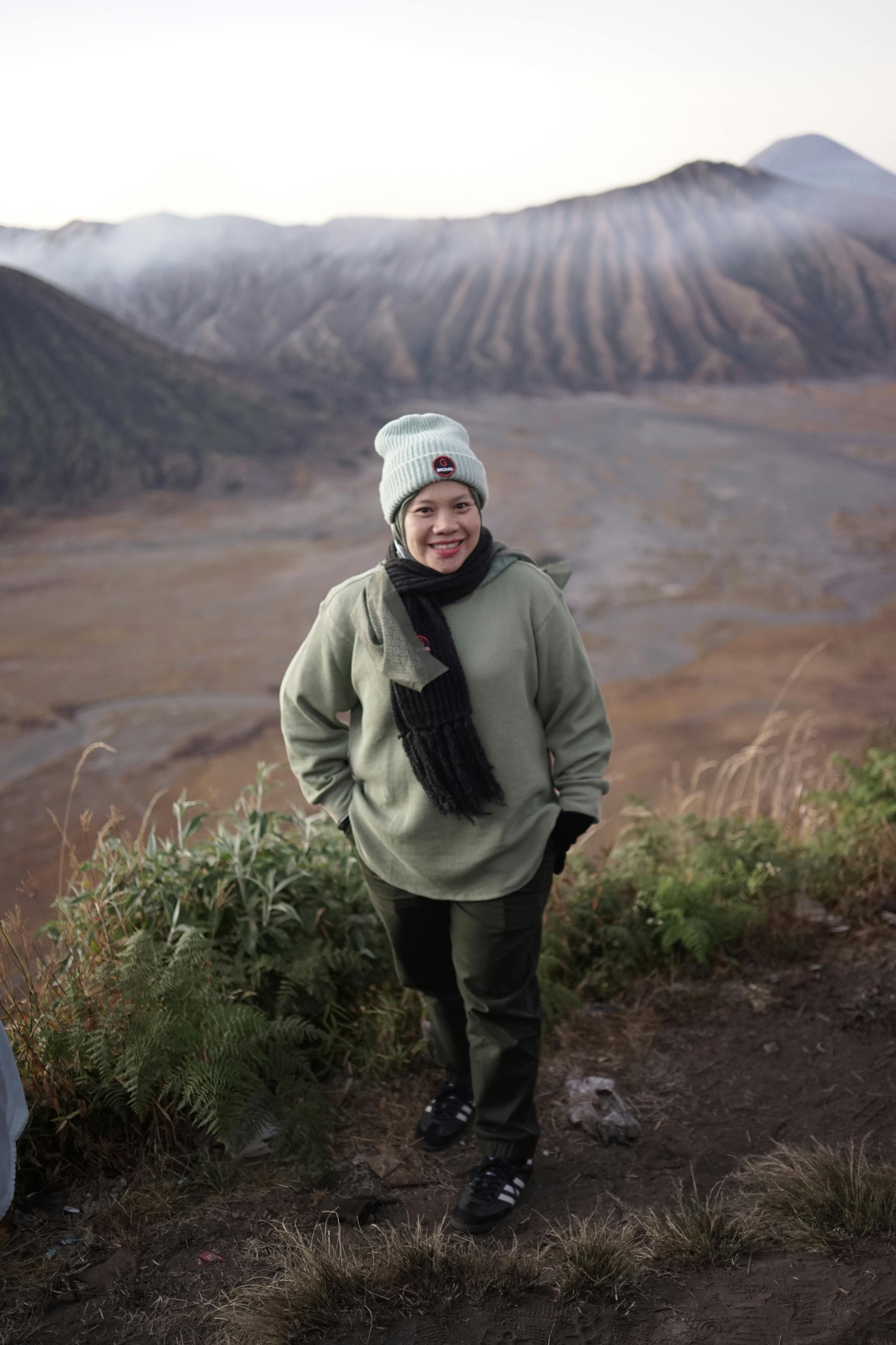 A woman dressed warmly overlooks a stunning mountain landscape in autumn, capturing leisure and nature.