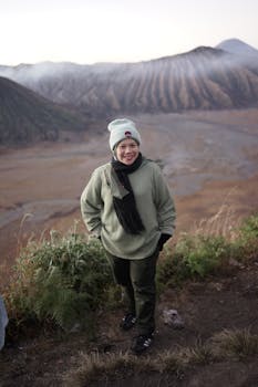 A woman dressed warmly overlooks a stunning mountain landscape in autumn, capturing leisure and nature.