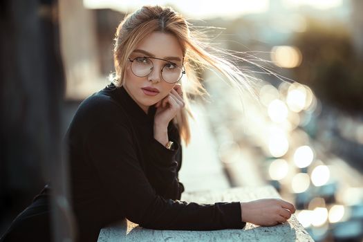 Elegant woman with eyeglasses posing outdoors with bokeh effect.