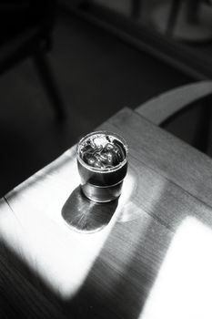 A minimalist black and white photo featuring an espresso cup casting a shadow on a wooden table.