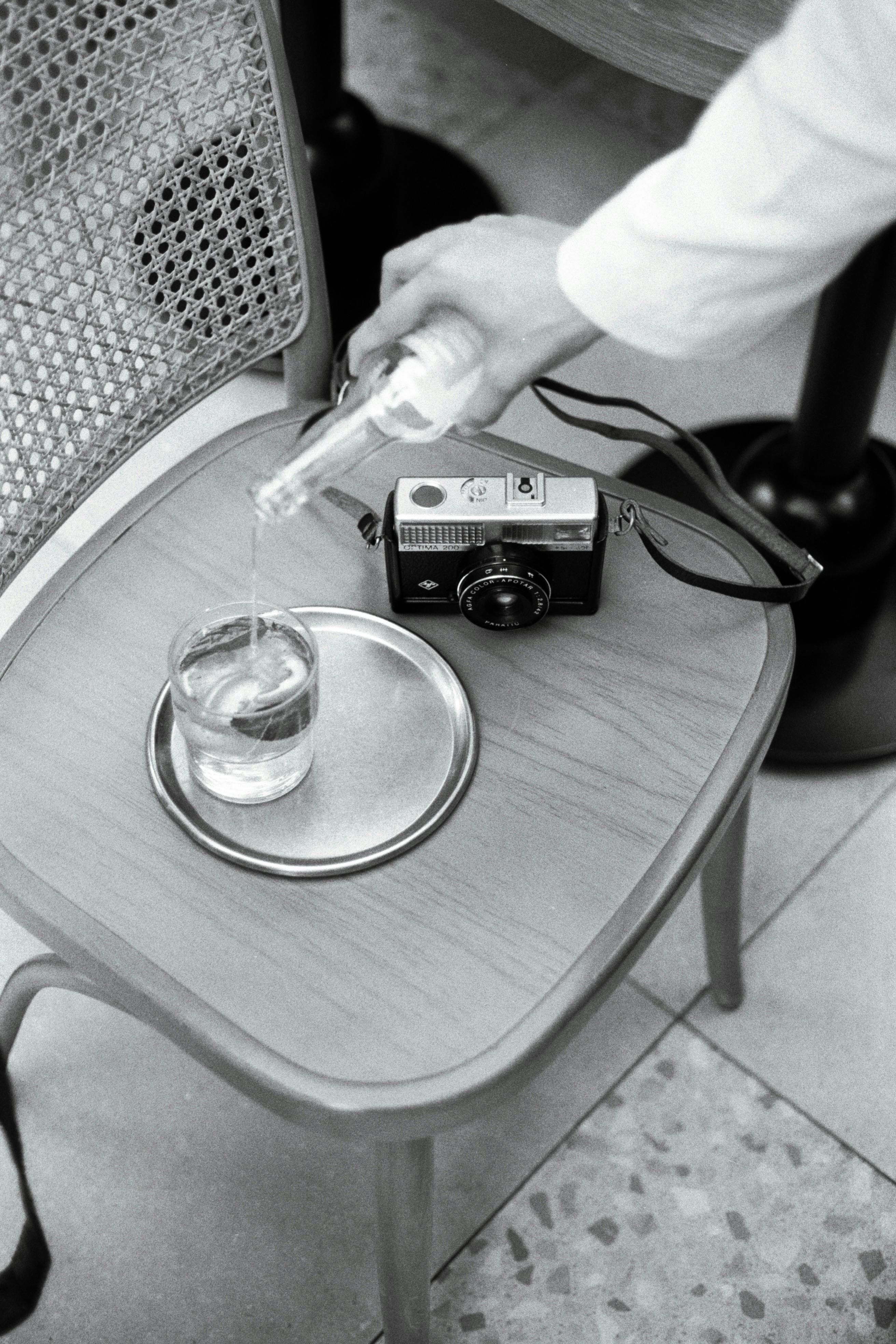 A vintage camera and a glass of water on a wooden chair, captured indoors with a retro feel.