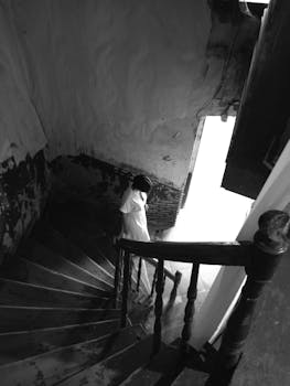 A solitary figure descending a dimly lit spiral staircase in a vintage setting.