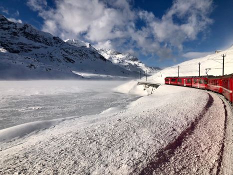 Red train navigating snow-covered mountains, offering a breathtaking alpine winter view.