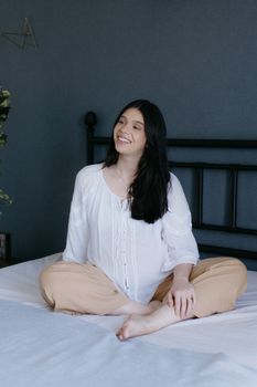 A serene portrait of a smiling woman in a relaxed pose on a bed indoors.