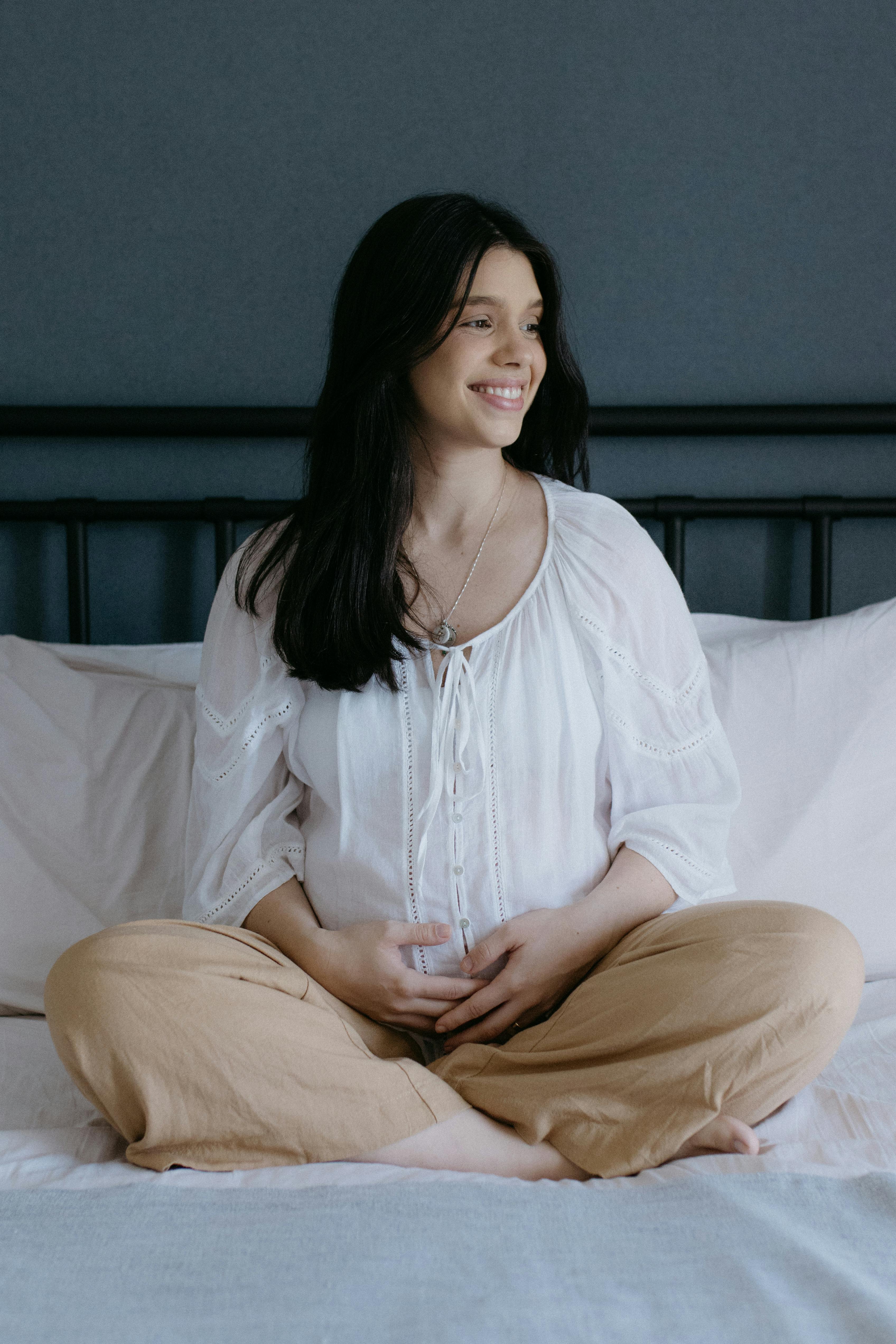 a pregnant woman sitting on a bed smiling