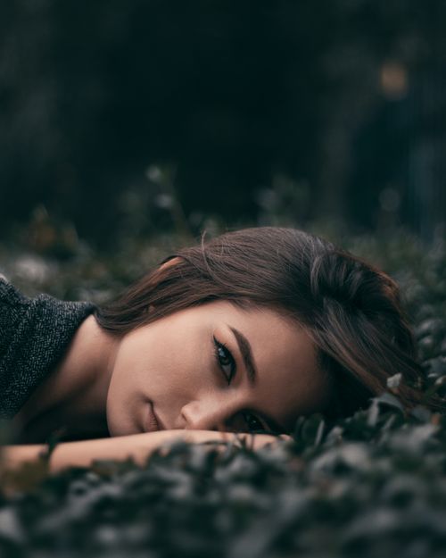 Free Artistic portrait of a woman with brunette hair lying on leaves, capturing an intimate and moody vibe. Stock Photo