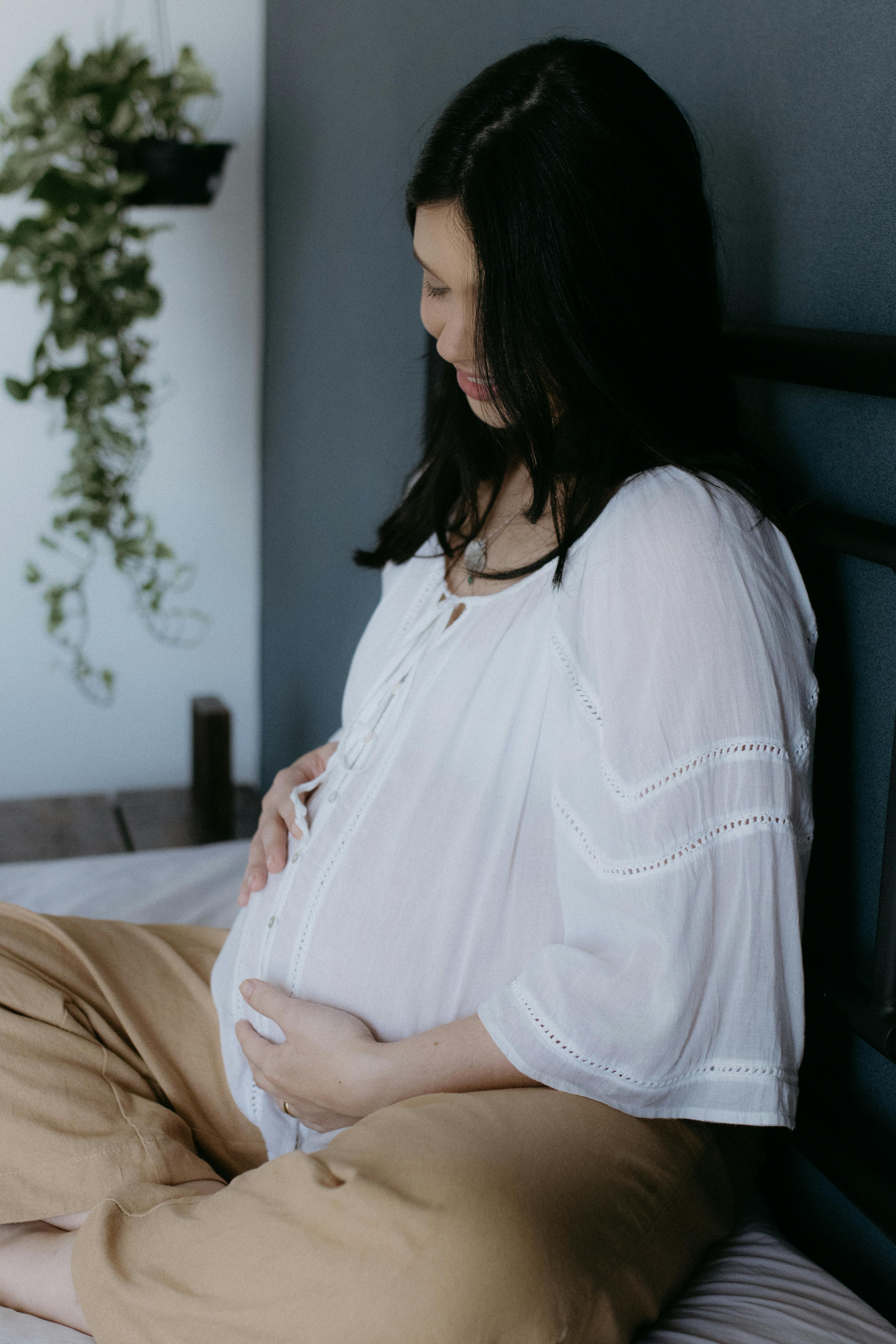 a pregnant woman sitting on a bed with her hands on her stomach