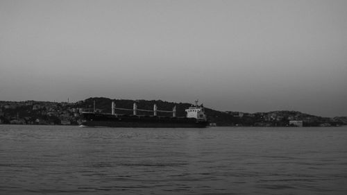 Free A large cargo ship glides silently across the calm sea at dusk, silhouetted against a distant shoreline. Stock Photo