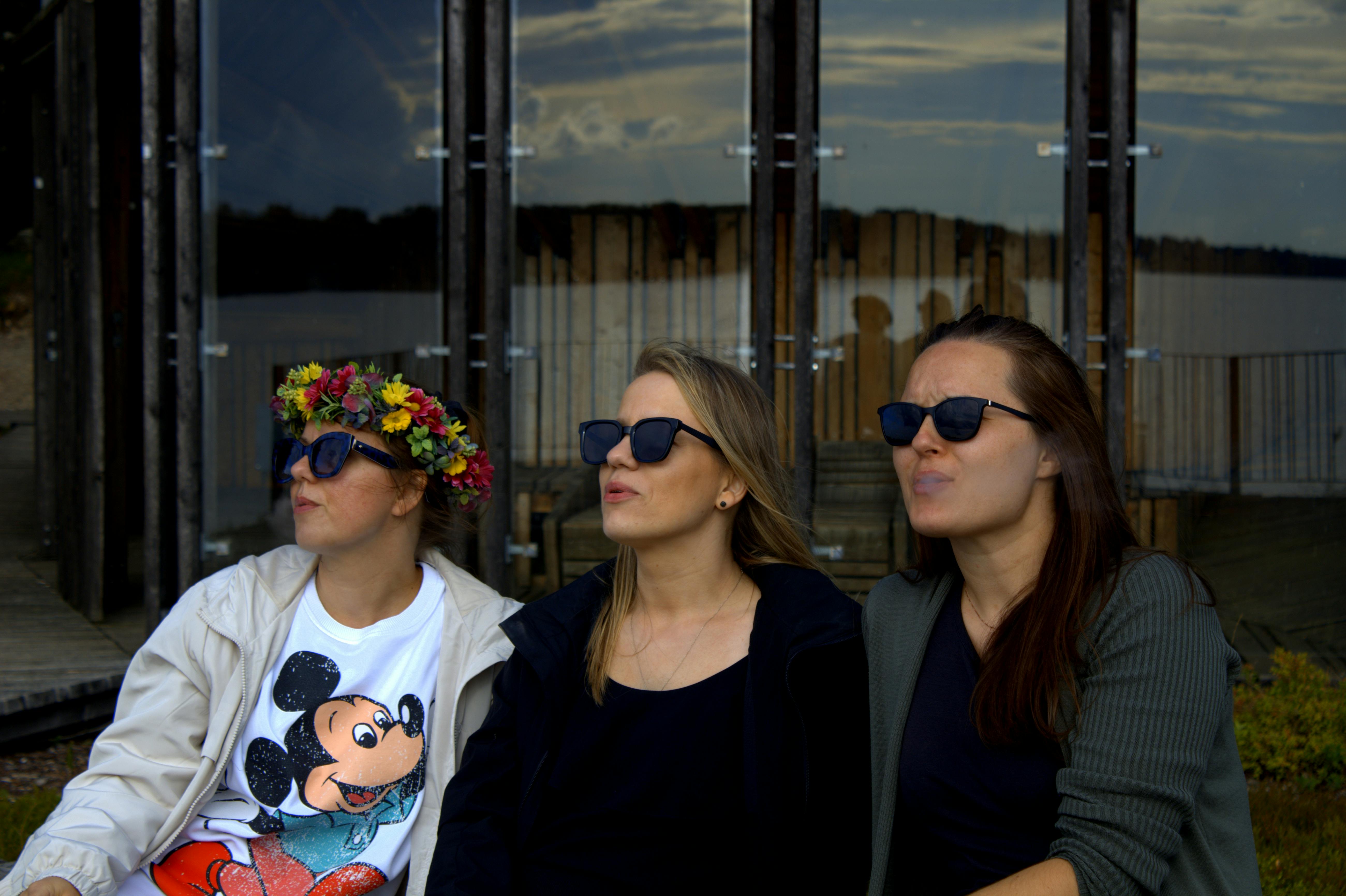 three women wearing sunglasses and earrings sit on a bench