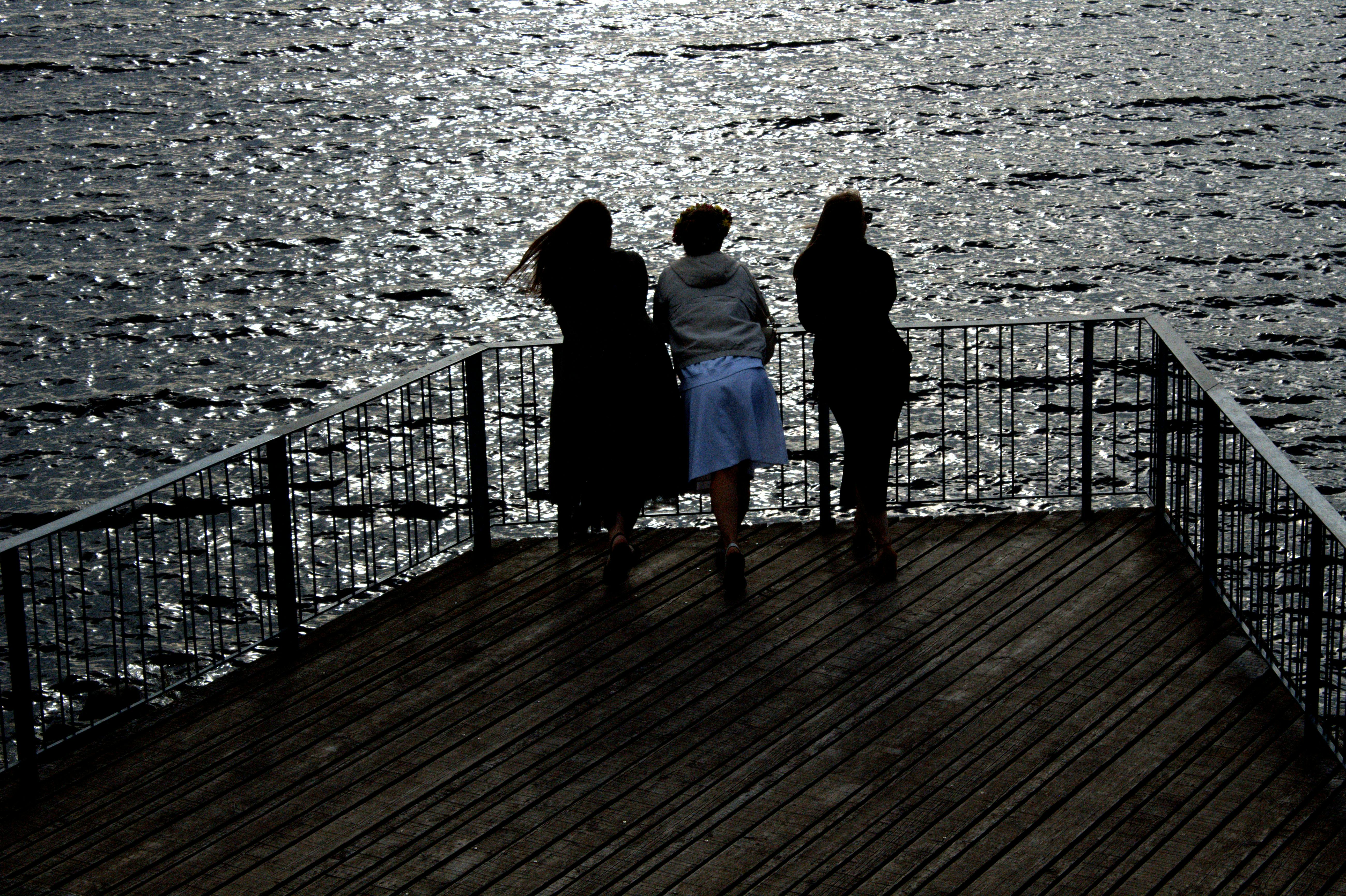 three women are standing on a pier looking at the water