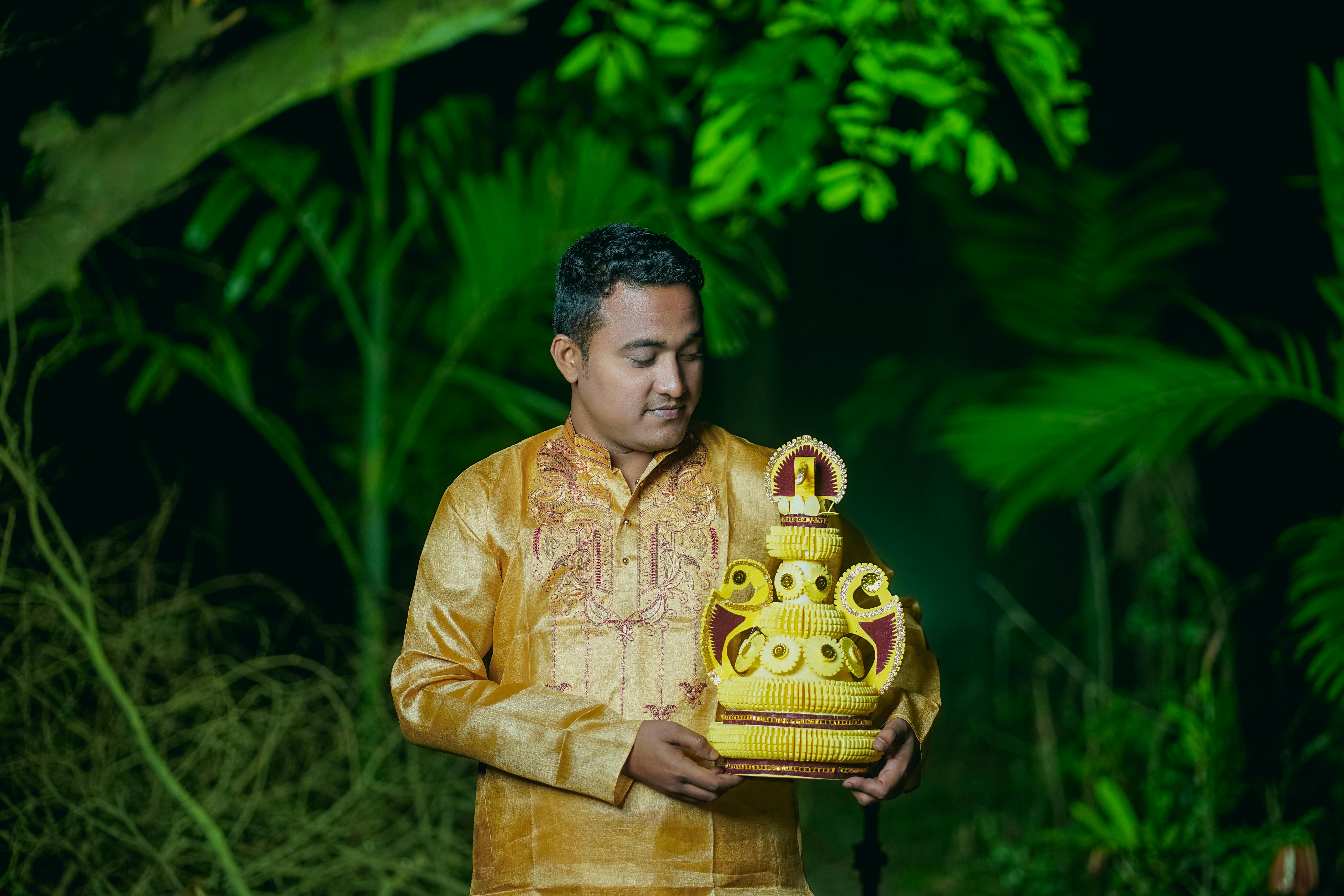 South Asian man in traditional attire holding an ornament in a vibrant green garden at twilight.