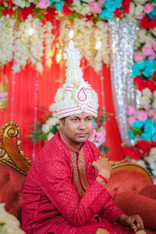 Free A Bengali groom adorned in traditional attire seated amidst colorful floral decorations. Stock Photo