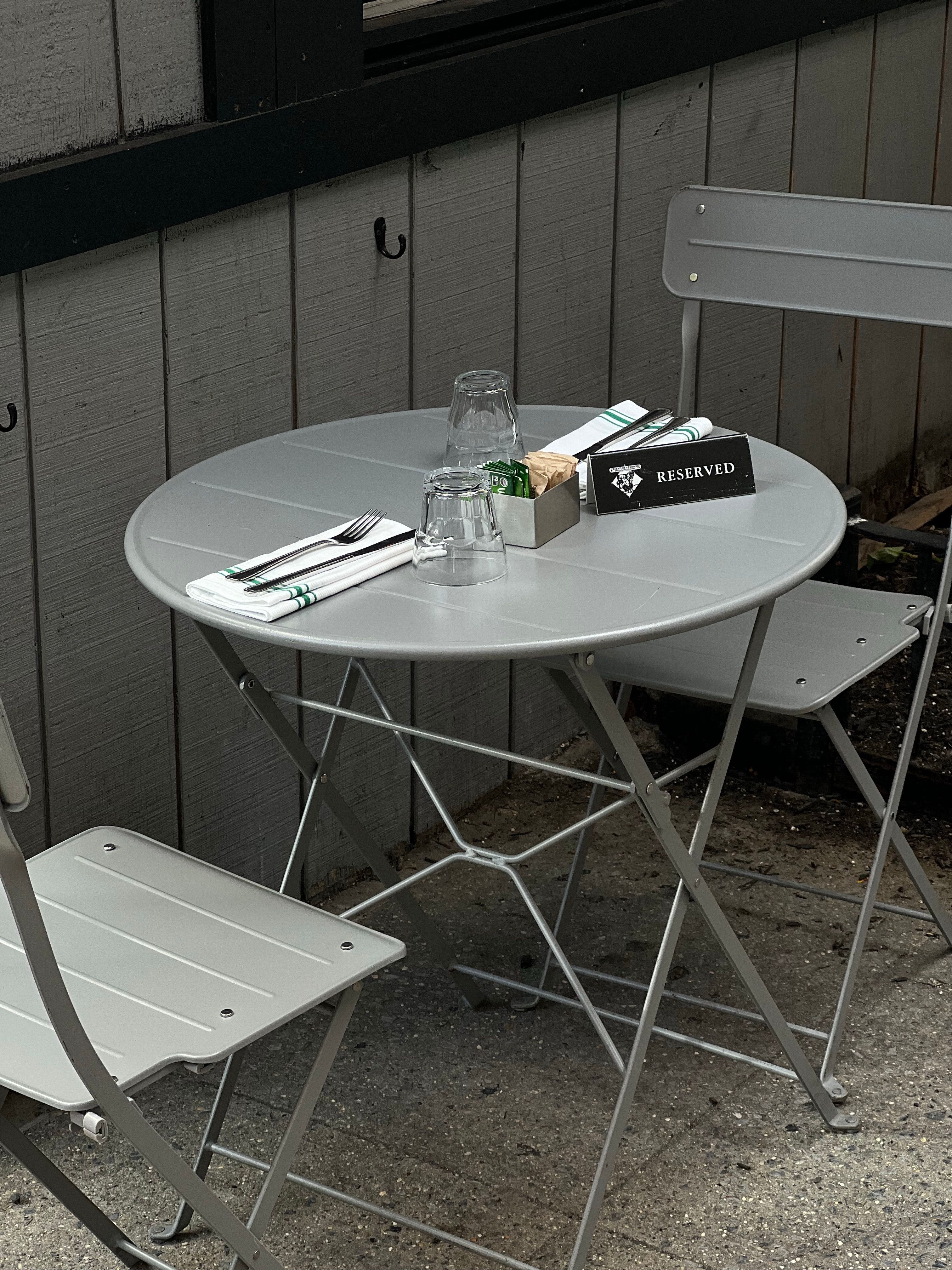 Side patio design with a small metal bistro set and striped umbrella placed on a paver patio