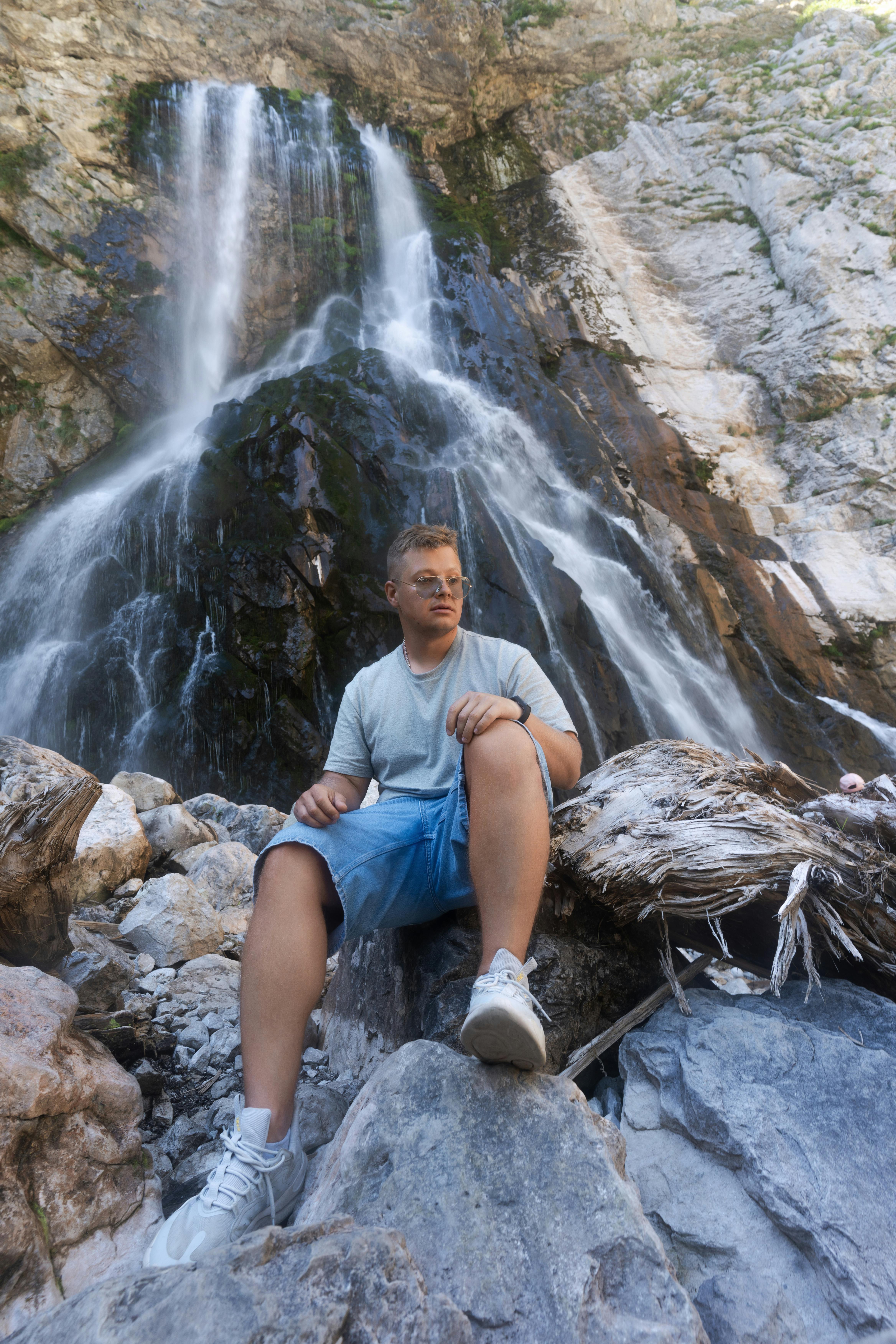 a man sitting on rocks next to a waterfall