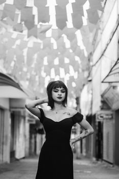 Stylish woman in black dress posing confidently in a vibrant urban street setting.