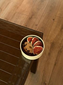 A bowl of fresh figs with granola on a rustic wooden table, capturing a cozy indoor setting.