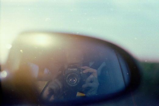 Capturing a film camera reflection in a car side mirror, showcasing vintage photography style.