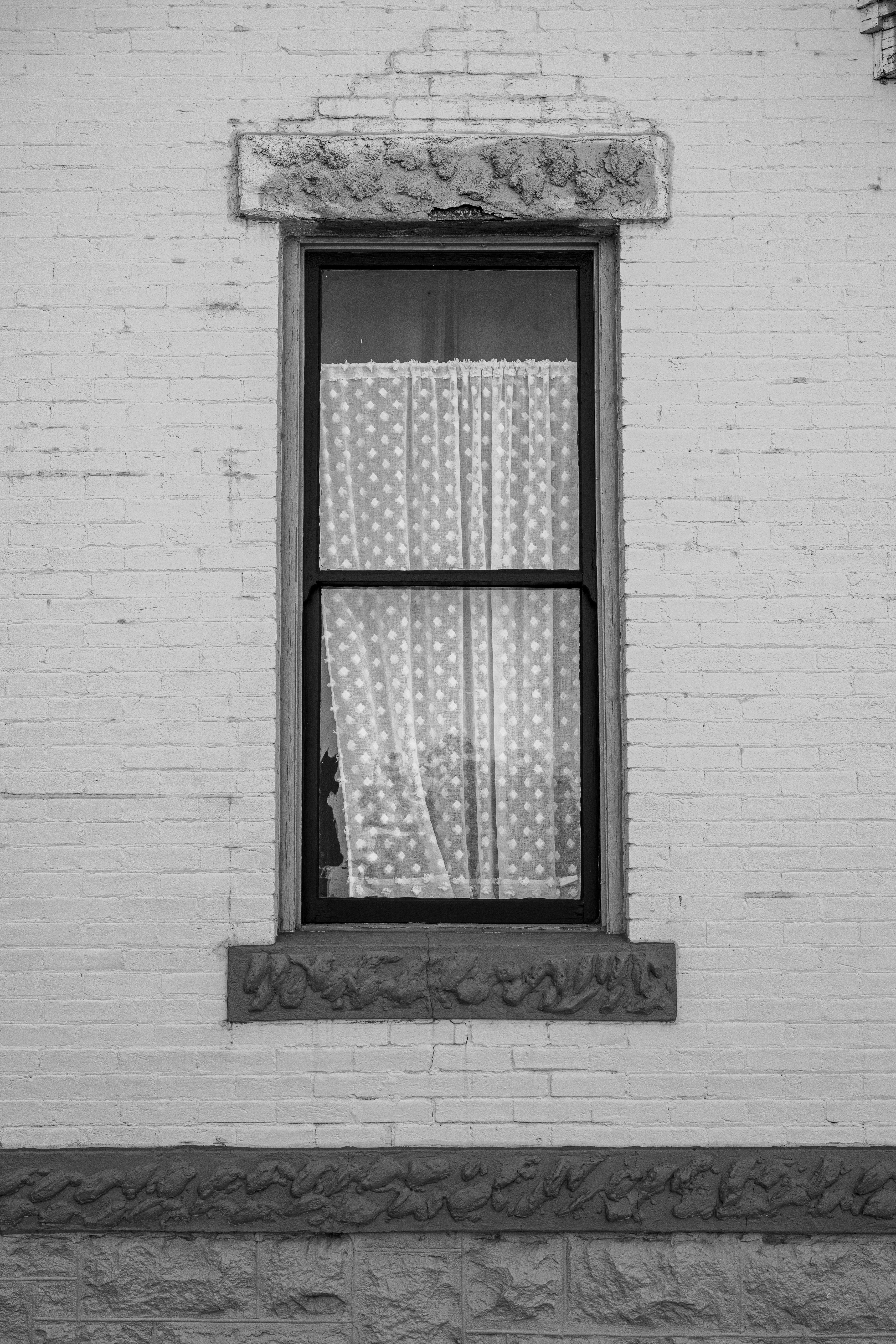 A rustic window with polka dot curtains set in a textured brick wall. Black and white photograph.