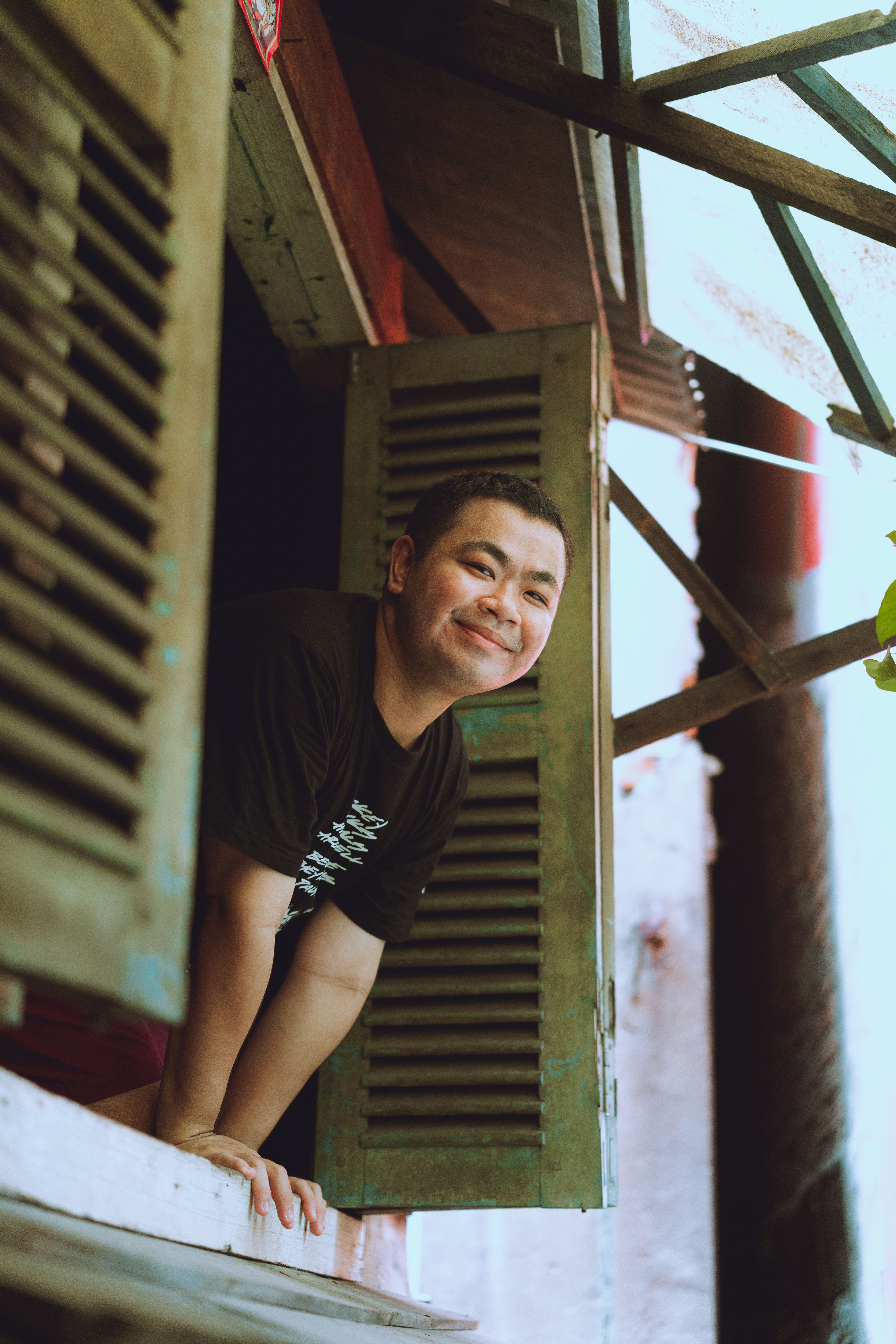 A smiling man leans out of a traditional wooden window in Ho Chi Minh City, Vietnam.
