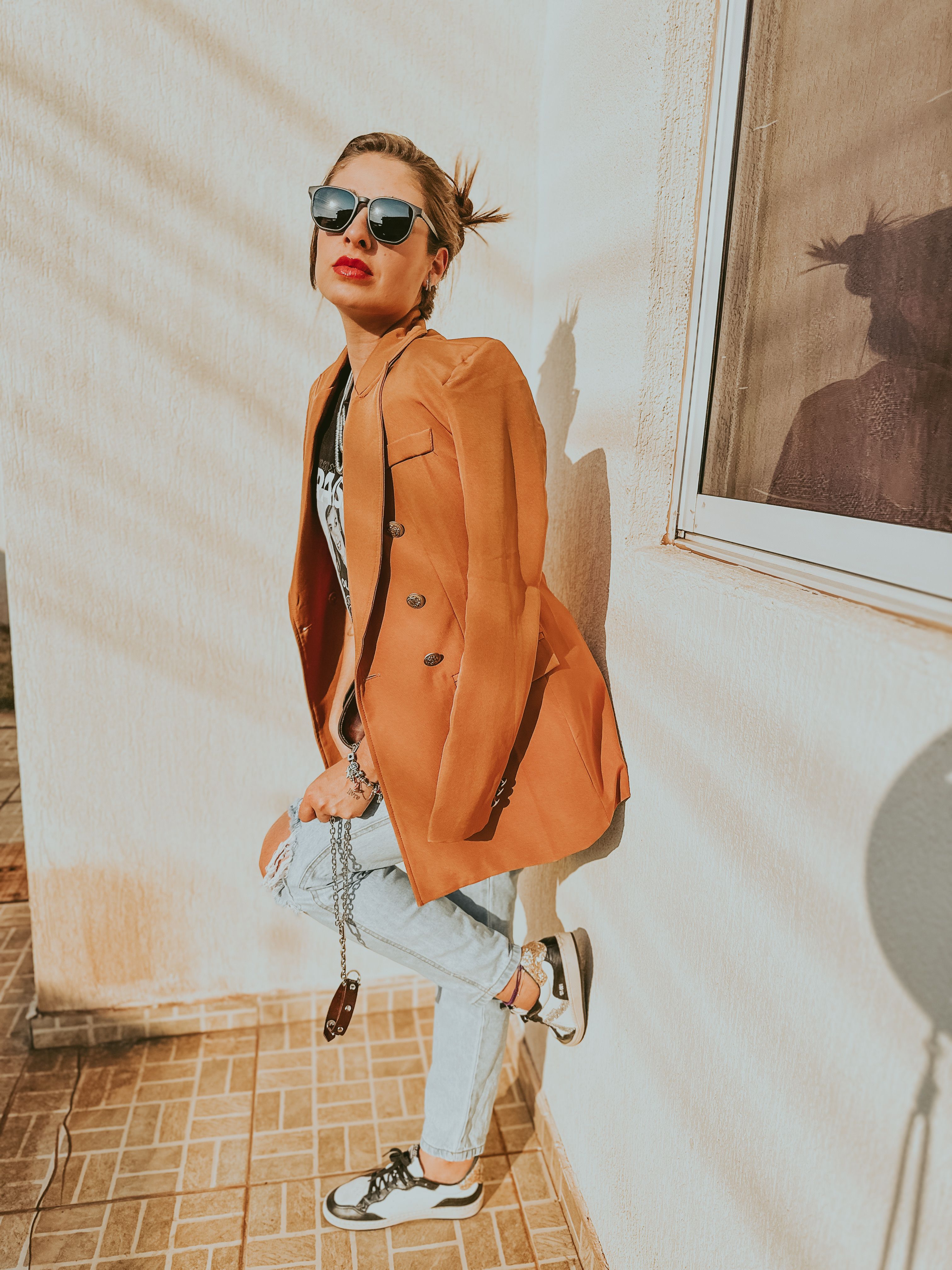Mulher jovem e fashionista de óculos de sol posando contra uma parede ensolarada em estilo retrô.