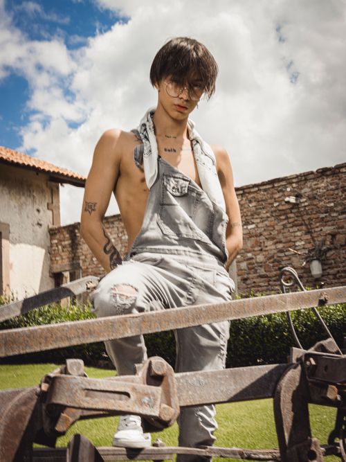 Free A young person poses in trendy overalls amidst a rustic outdoor backdrop. Stock Photo