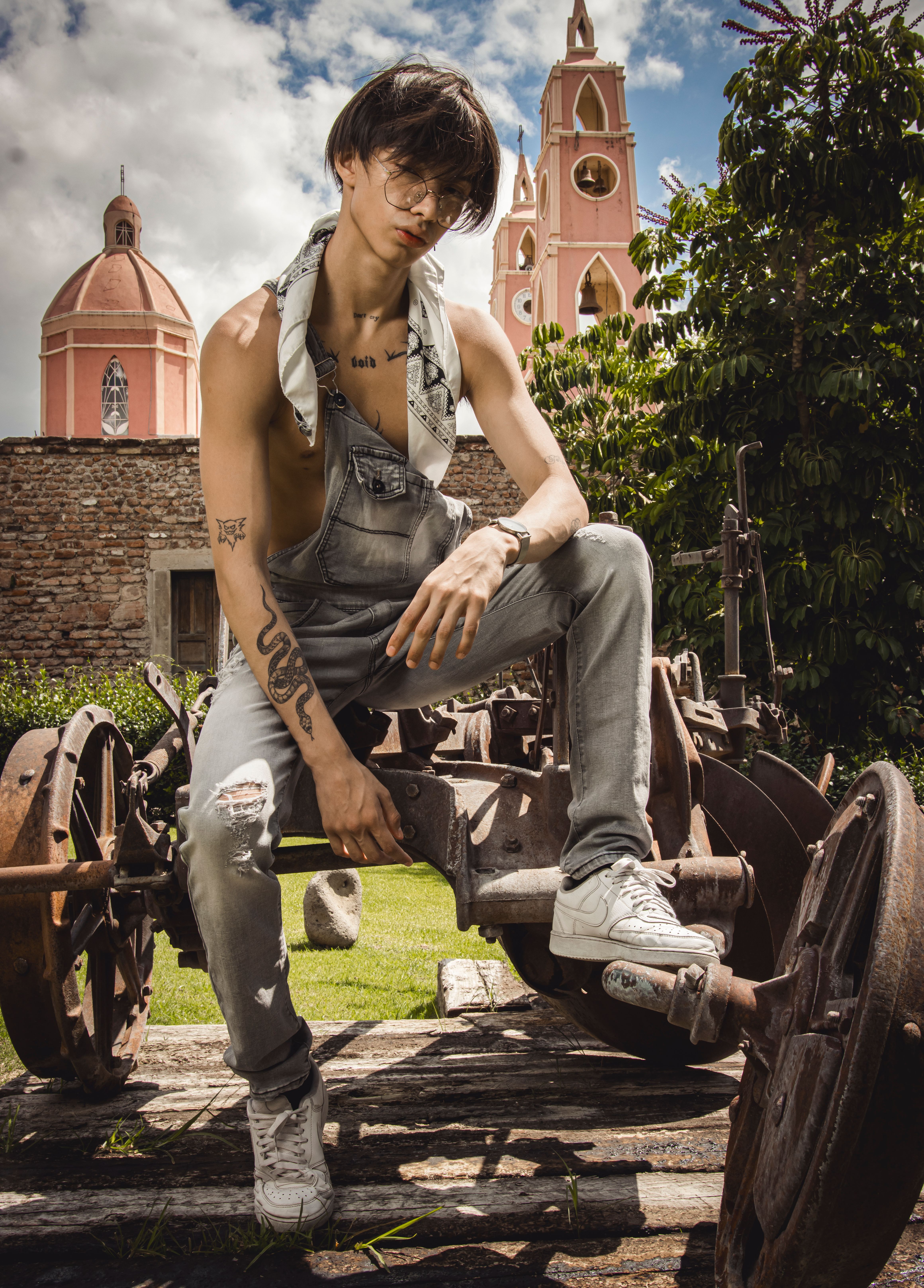 Fashionable young man with tattoos posing on vintage machinery outdoors.