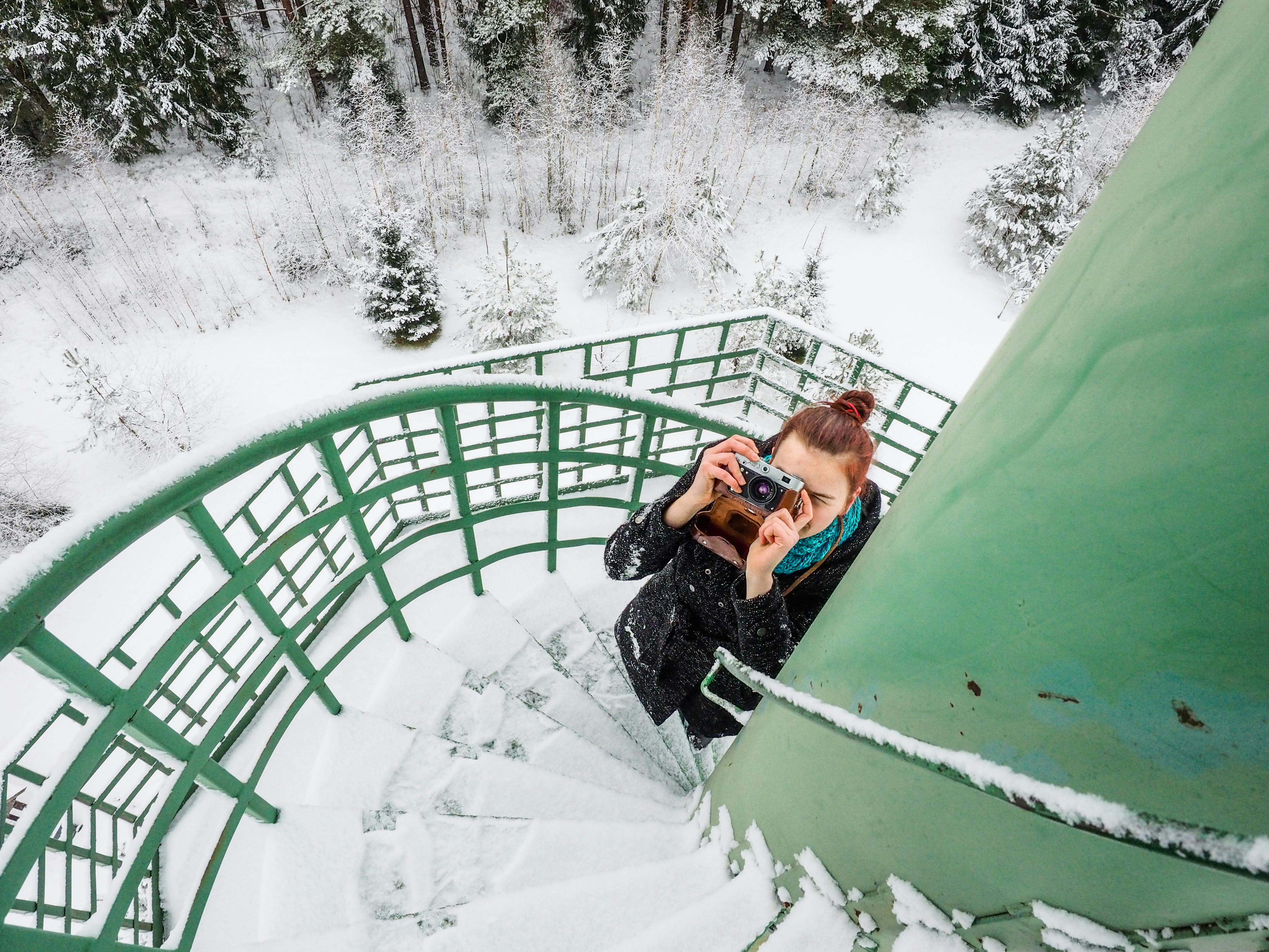 在立陶宛扎拉赛的积雪中，一名女子带着相机走上冰冷的螺旋楼梯