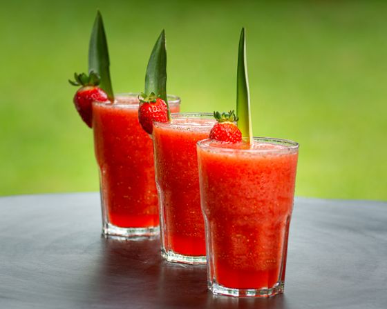 Three glasses of red frozen strawberry slush garnished with strawberries and pineapple leaves