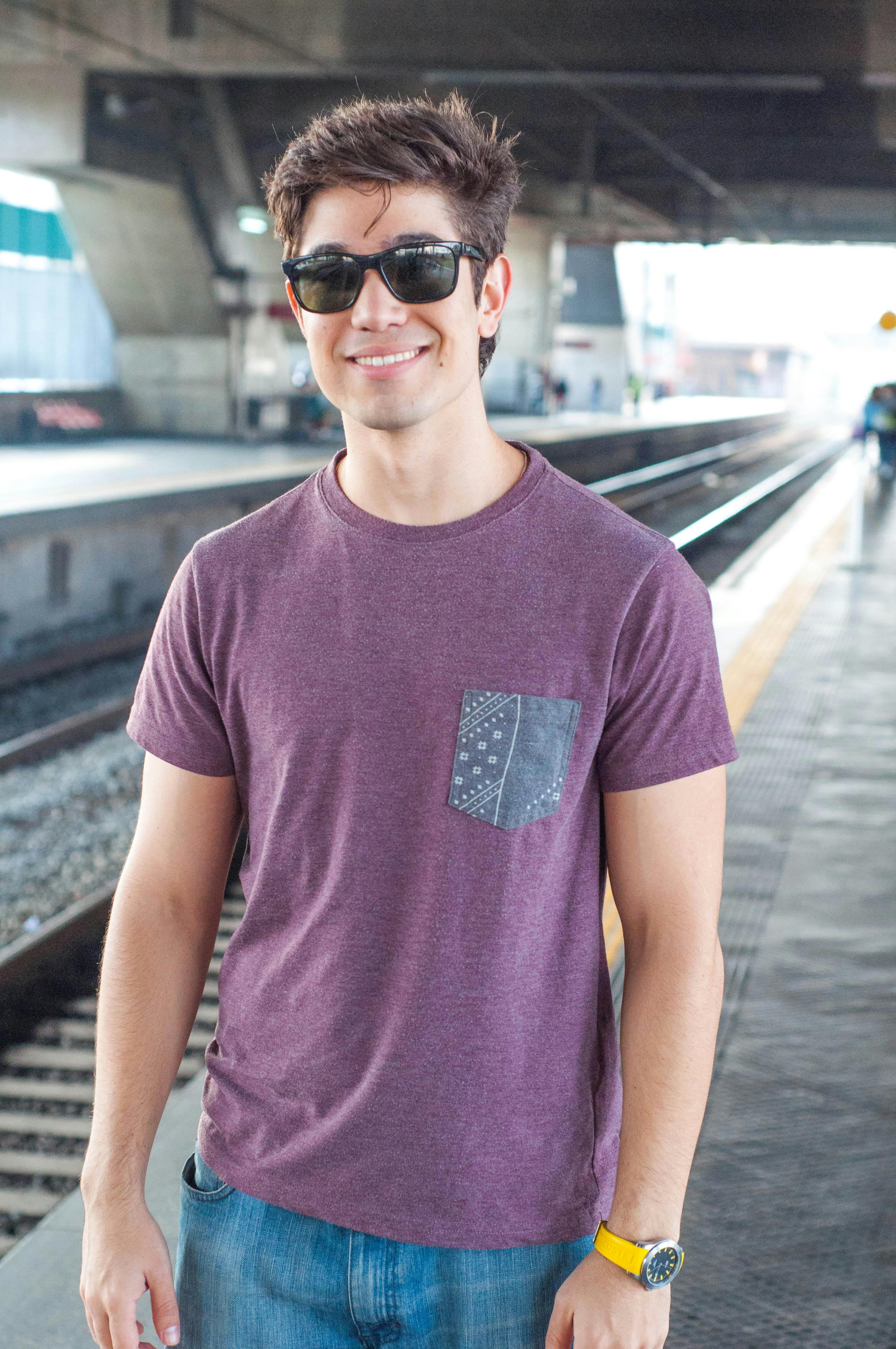 Smiling young man in sunglasses waiting at a train station platform.