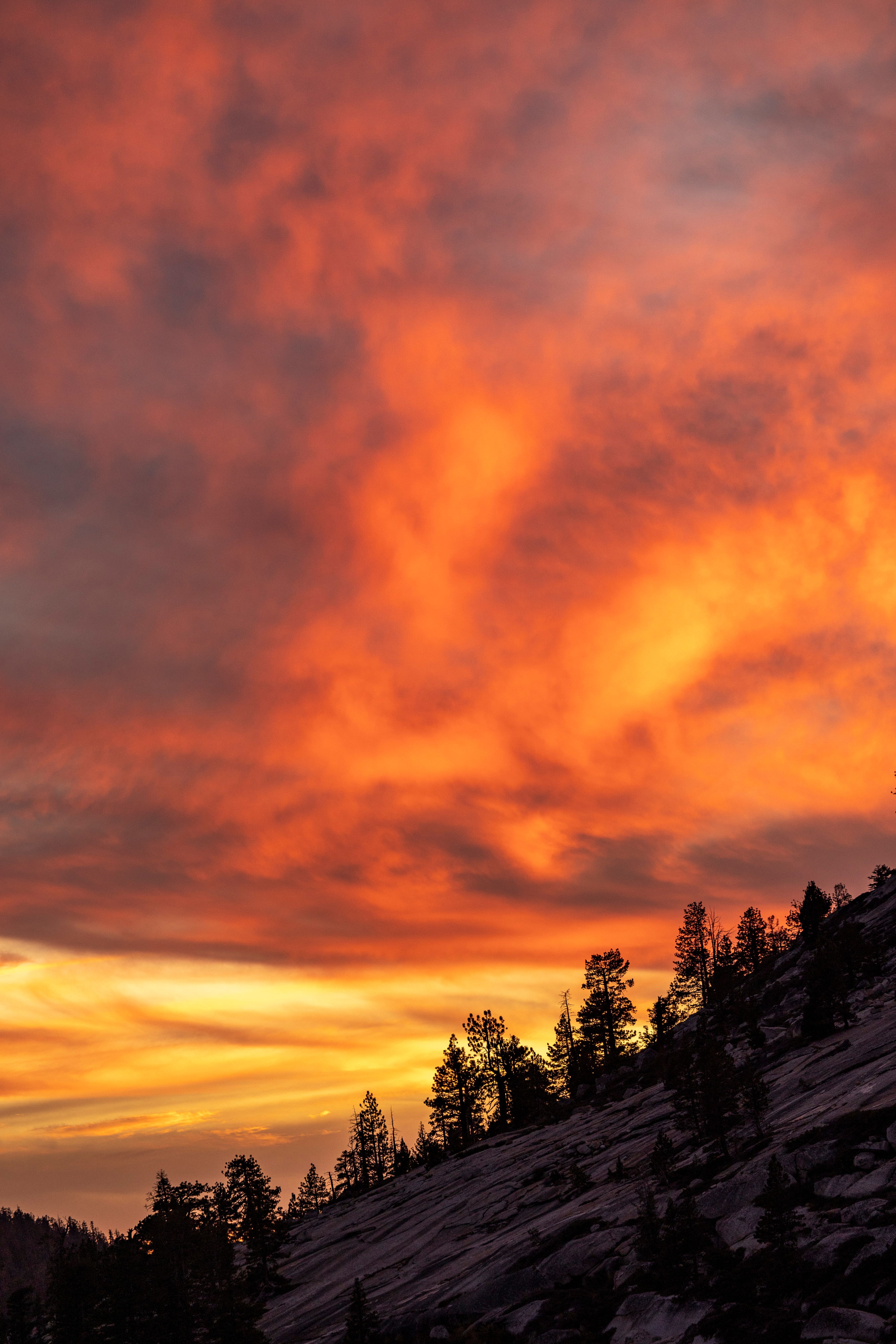 A sunset over a mountain with clouds and trees · Free Stock Photo