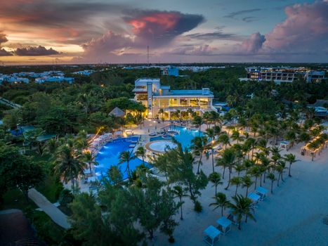 Aerial view of a stunning beach resort in Playa del Carmen at sunset, showcasing vibrant skies and luxurious amenities.