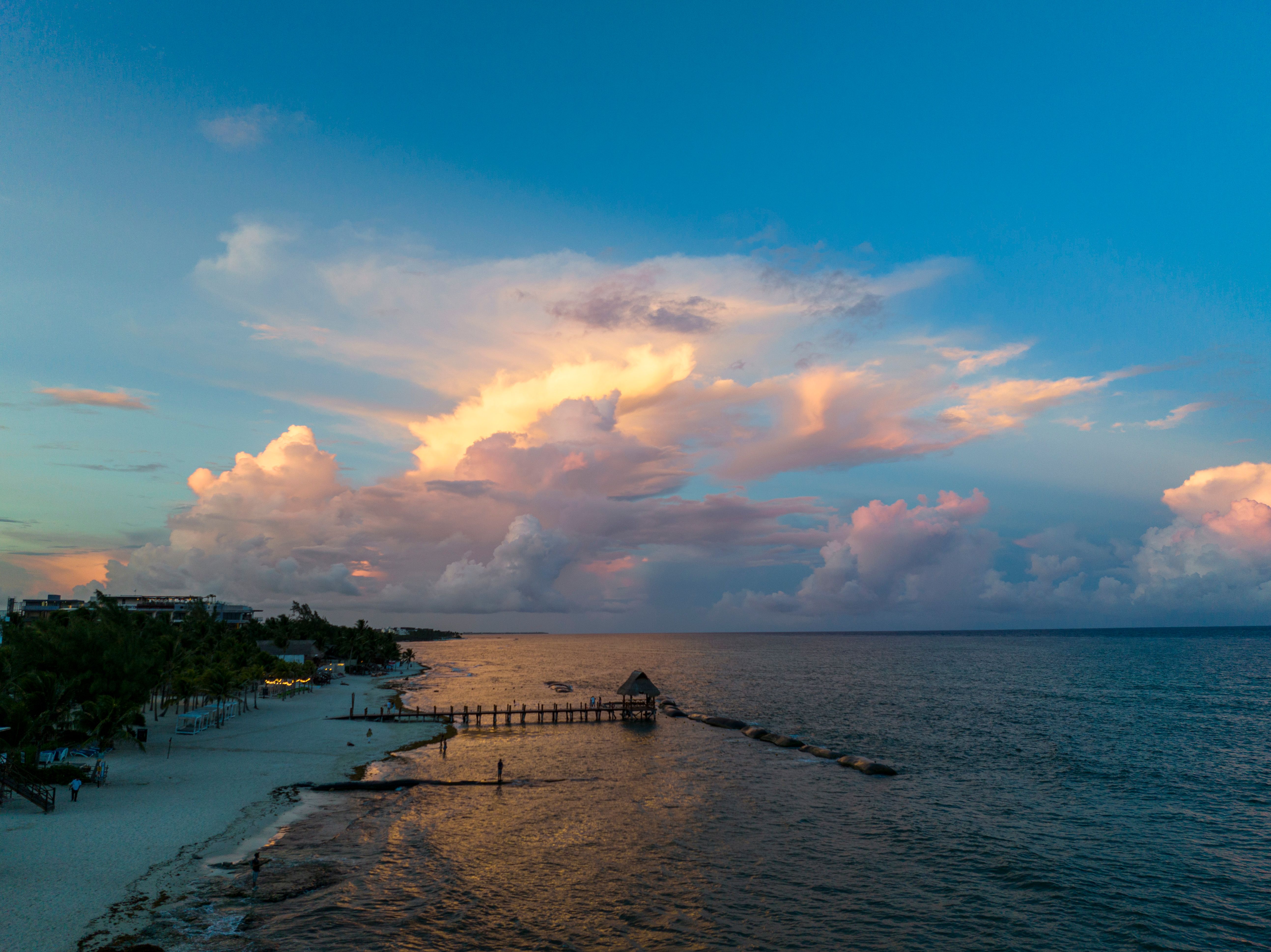 A beach with a pier and clouds in the sky · Free Stock Photo