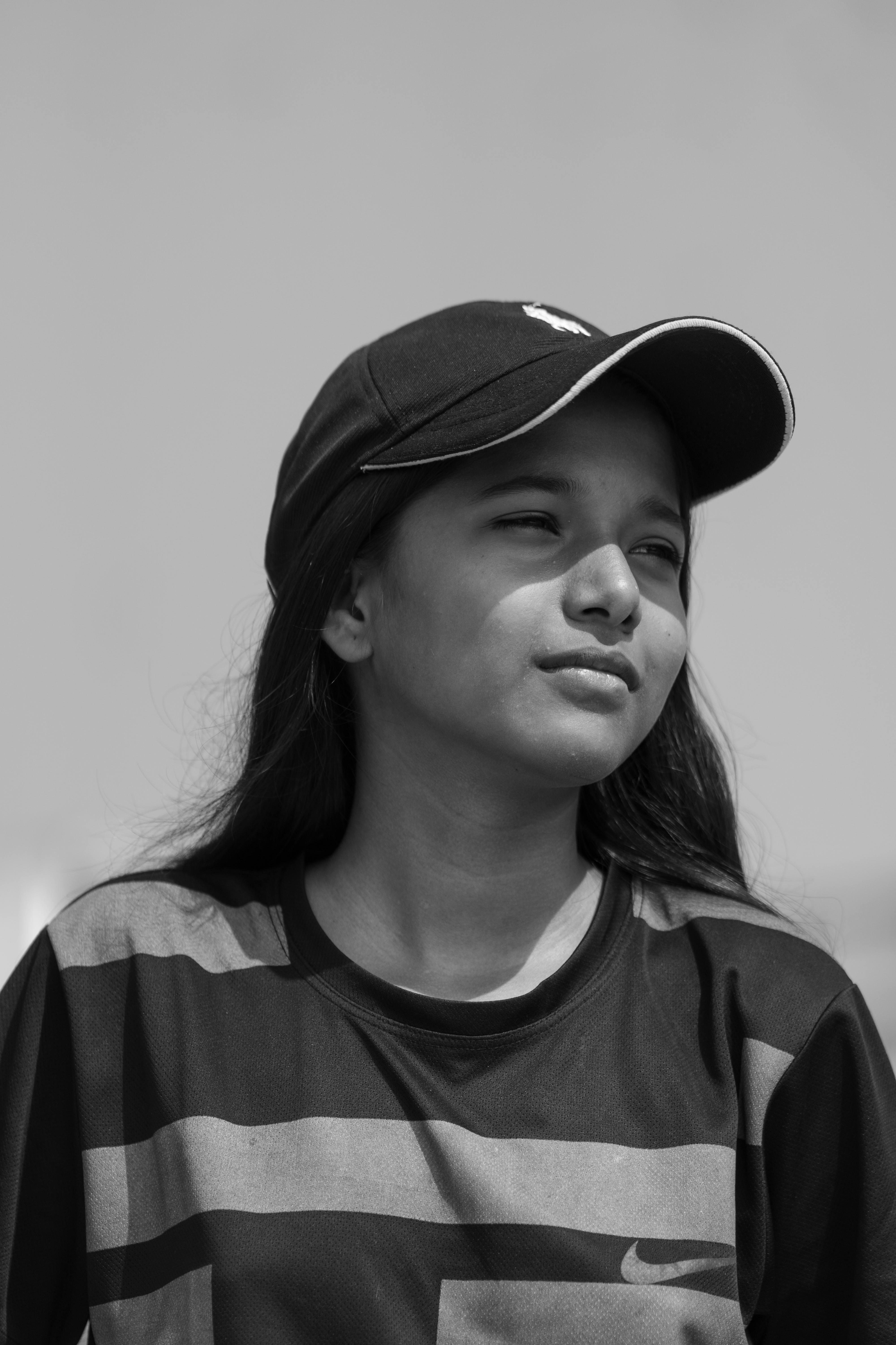 a black and white photo of a girl wearing a baseball cap