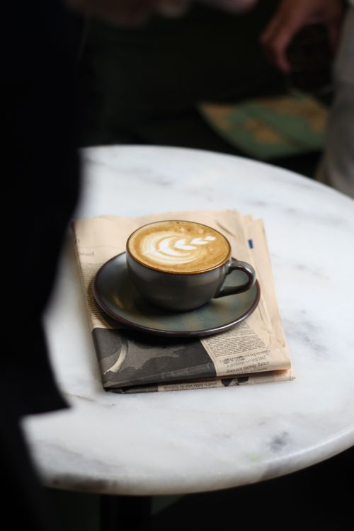 Free A steaming cappuccino on a newspaper atop a marble table, perfect for mornings. Stock Photo