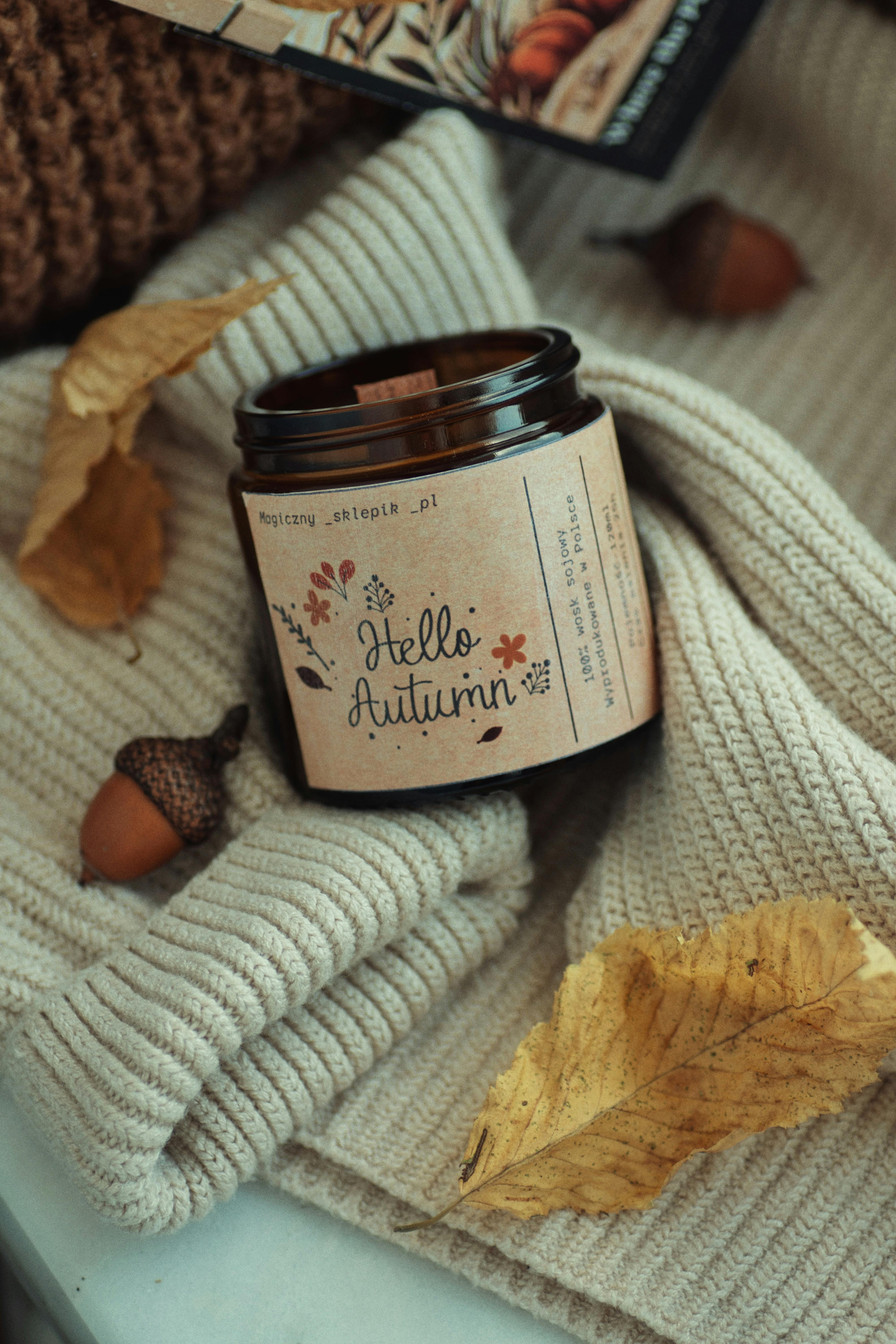 Warm autumn scene with a candle, sweater, and fallen leaves for relaxation and comfort.